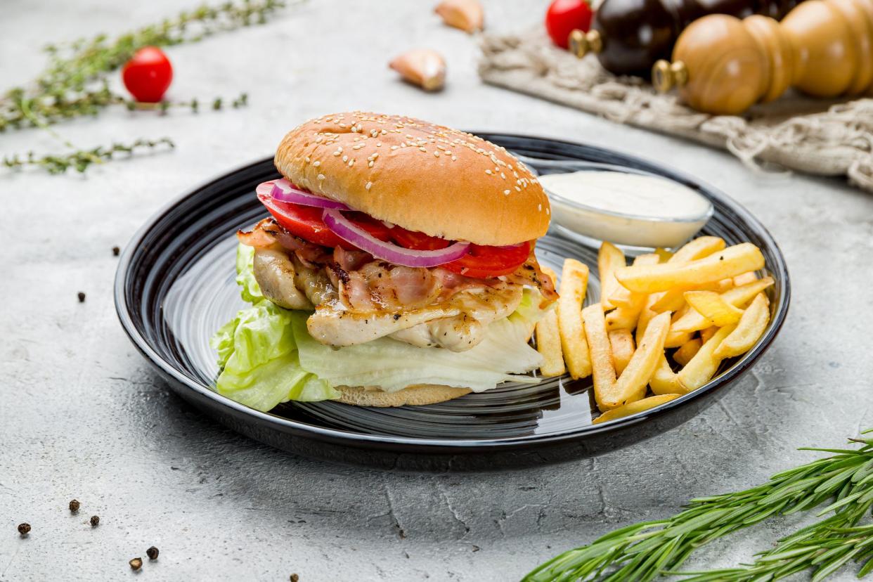 Burger with chicken, bacon,salad,tomatoes with french fries and sauce on plate