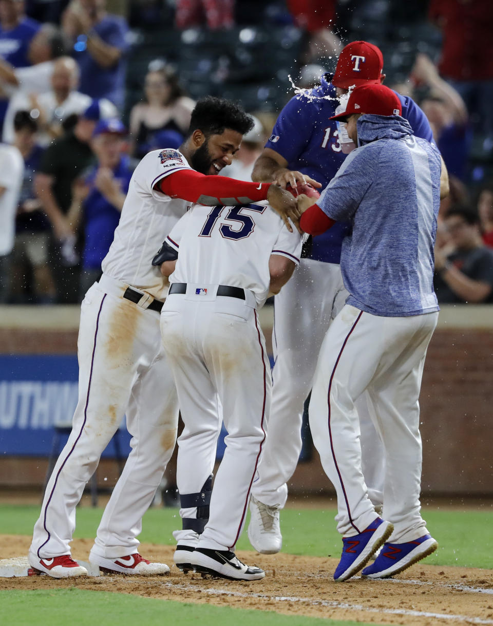 Texas Rangers' Nick Solak (15) is greeted by Elvis Andrus, left, Nomar Mazara, rear, and Jose Trevino, right, after Solak reached first on a fielding error by Los Angeles Angels' Albert Pujols that allowed Delino DeShields to score in the 11th inning of a baseball game in Arlington, Texas, Tuesday, Aug. 20, 2019. The Rangers won 3-2. (AP Photo/Tony Gutierrez)