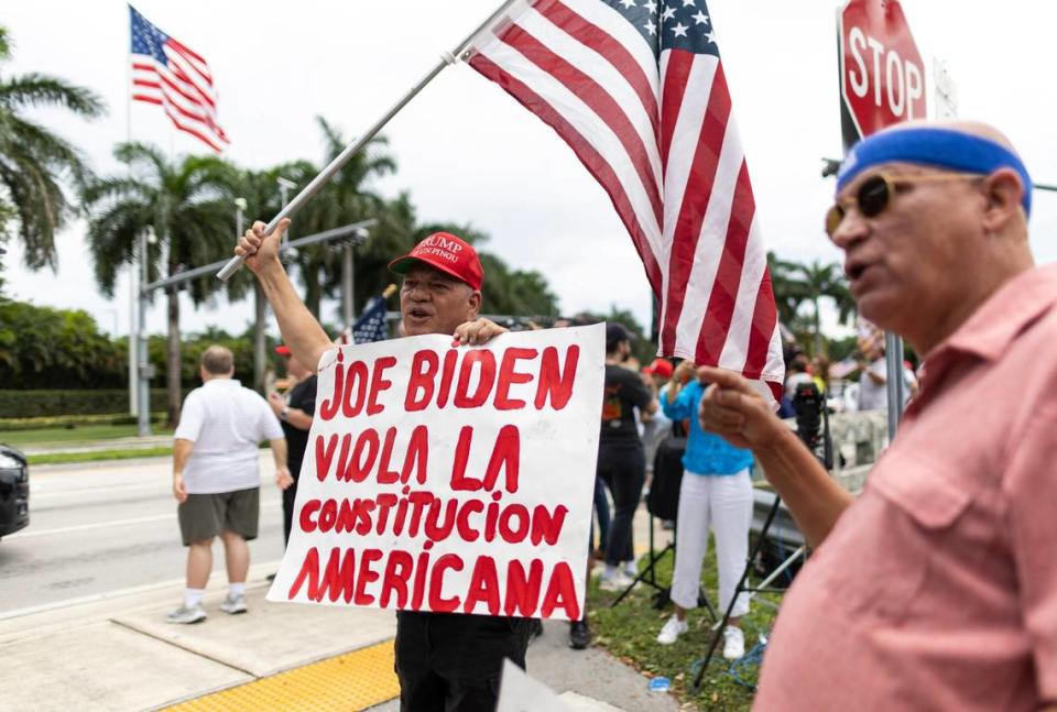 Joel Talavera, center, holds a flag and a sign while standing outside Trump National Doral on Monday, June 12, 2023, in Doral, Fla.