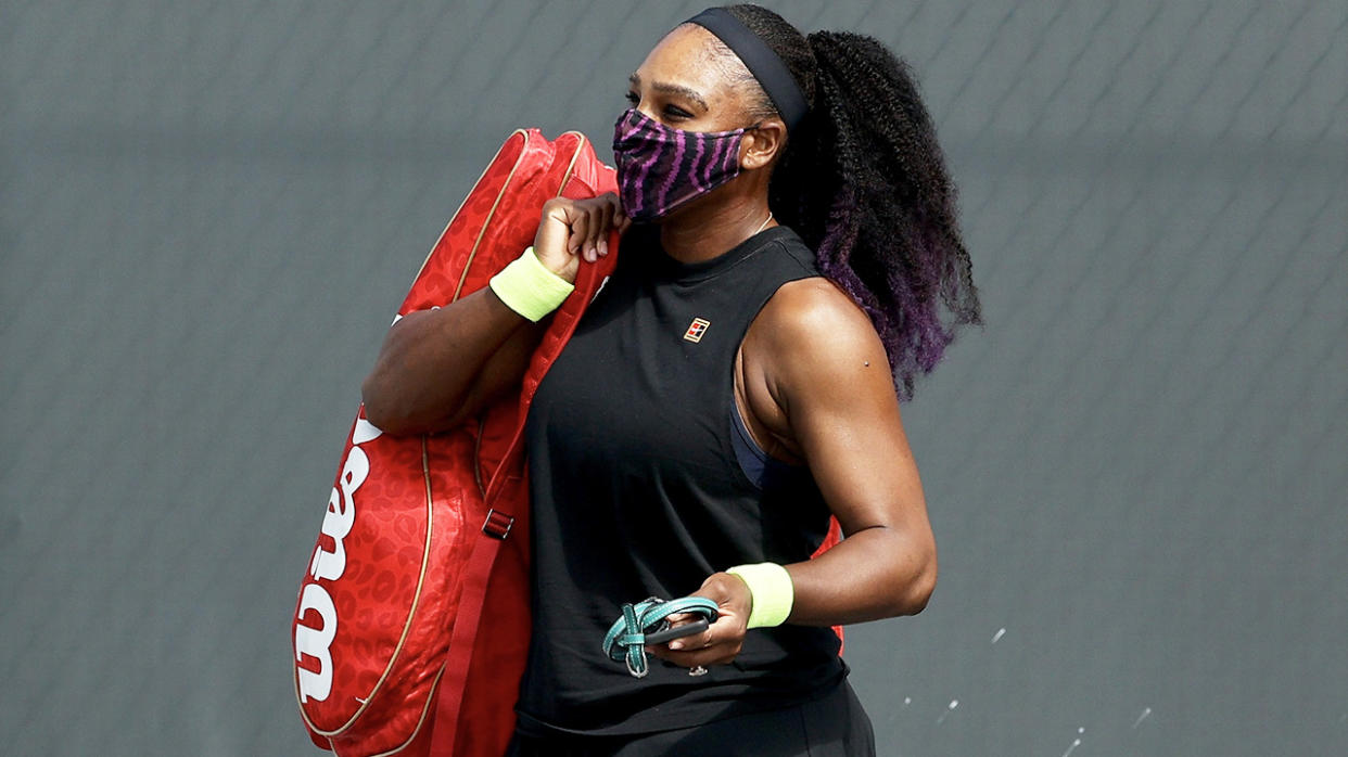 Serena Williams walks across the court with a mask and carrying her bag.