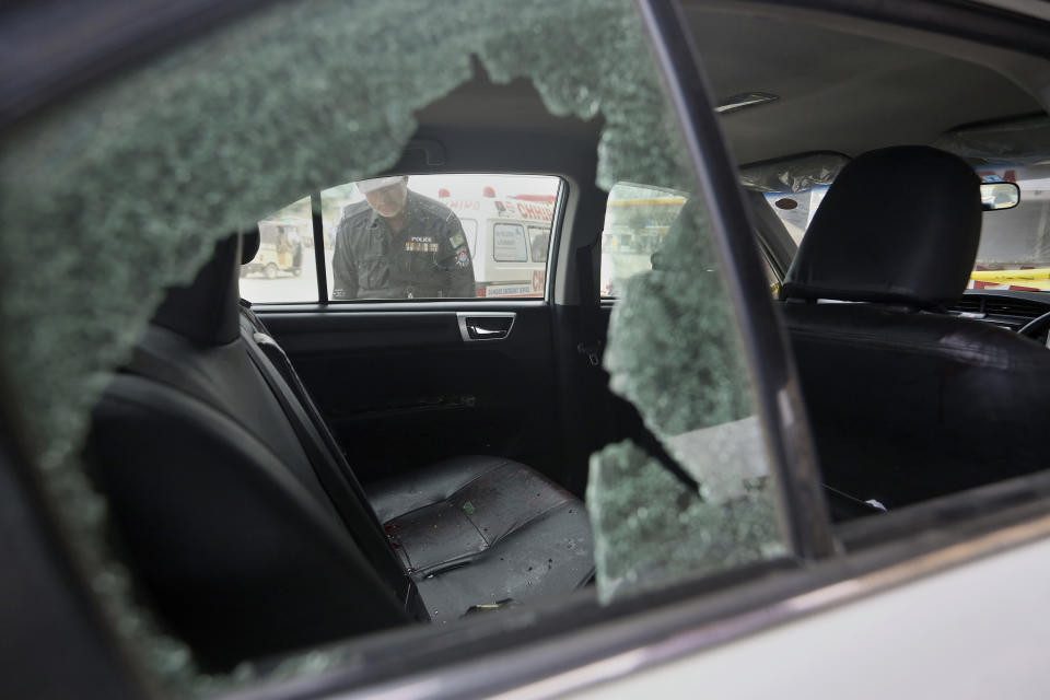 A police officer examines a damaged car at the site of a firing incident, in Karachi, Pakistan, Wednesday, July 28, 2021. Gunmen riding on a motorcycle fired into the car carrying two Chinese factory workers in Pakistan's port city of Karachi on Wednesday, wounding one of them before fleeing the scene, a rescue official and police said. (AP Photo/Fareed Khan)