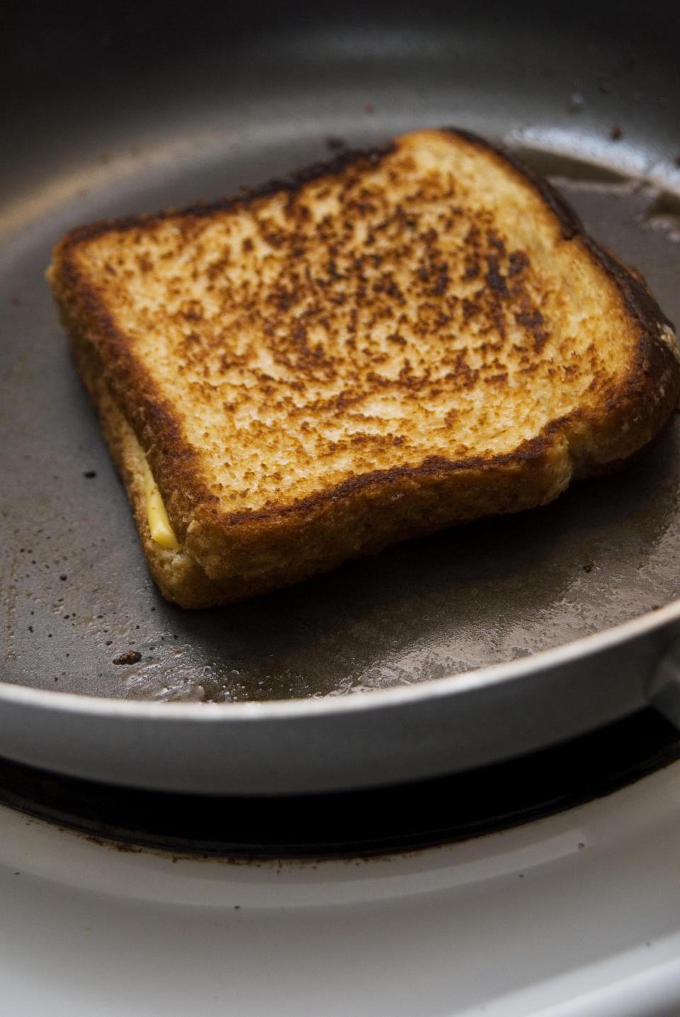 Close-up of a grilled cheese sandwich being cooked in a frying pan. The bread is toasted with visible grill marks