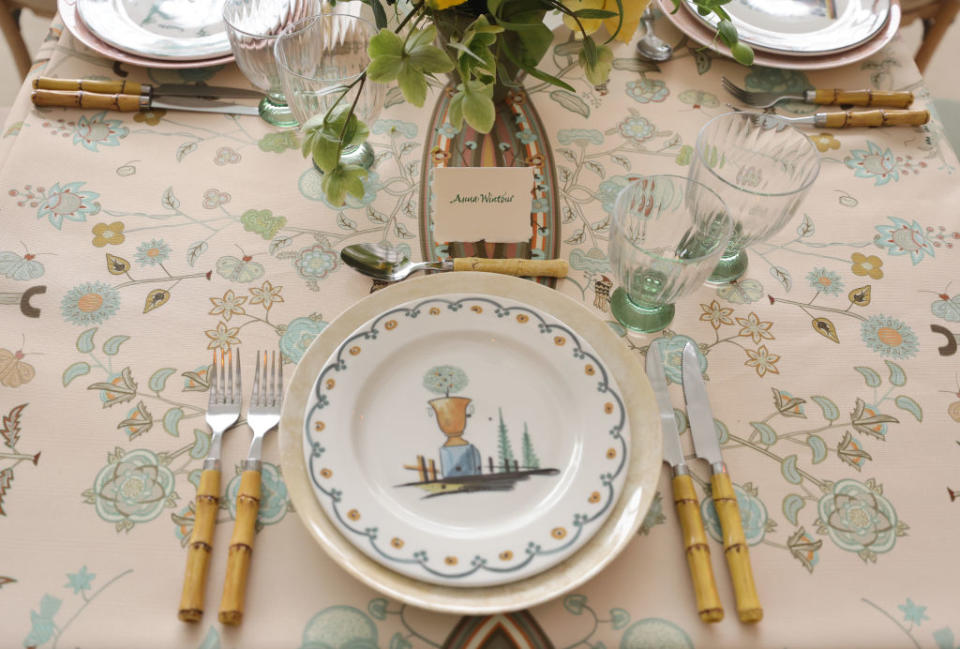 A table setting with a place card reading "Anna Wintour," floral dishes, and bamboo-style flatware