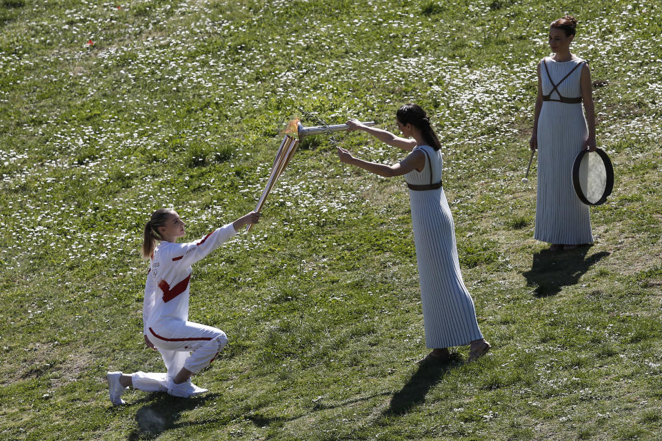 Greek actress Xanthi Georgiou, center, playing the role of the High Priestess, lights the torch of the 2020 Tokyo Olympic Games, held by Greek shooting Olympic champion Anna Korakaki, left, the first torchbearer, during the flame lighting ceremony at the closed Ancient Olympia site, birthplace of the ancient Olympics in southern Greece, Thursday, March 12, 2020, 2020. Greek Olympic officials are holding a pared-down flame-lighting ceremony for the Tokyo Games due to concerns over the spread of the coronavirus. Both Wednesday's dress rehearsal and Thursday's lighting ceremony are closed to the public, while organizers have slashed the number of officials from the International Olympic Committee and the Tokyo Organizing Committee, as well as journalists at the flame-lighting. (AP Photo/Yorgos Karahalis)