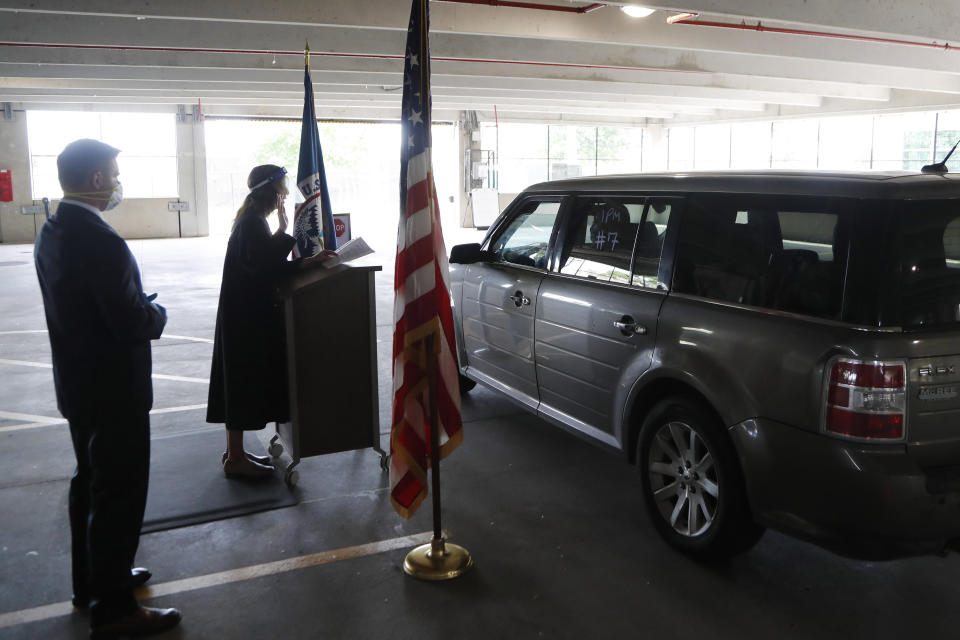 In this Friday, June 26, 2020 photo, U.S. District Judge Laurie Michelson, center, administers the Oath of Citizenship during a drive-thru naturalization service in a parking structure at the U.S. Citizenship and Immigration Services headquarters on Detroit's east side. The ceremony is a way to continue working as the federal courthouse is shut down due to Coronavirus. The U.S. has resumed swearing in new citizens but the oath ceremonies aren't the same because of COVID-19 and a budget crisis at the citizenship agency threatens to stall them again. (AP Photo/Carlos Osorio)