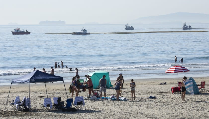 HUNTINGTON BEACH, CA - OCTOBER 03: Beachgoers at Newport Beach enjoy the afternoon as boats drag oil booms offshore on Sunday, Oct. 3, 2021. Authorities said 126,000 gallons of oil leaked from the offshore oil rig Elly on Saturday affecting Huntington Beach and Newport Beach. (Myung J. Chun / Los Angeles Times)