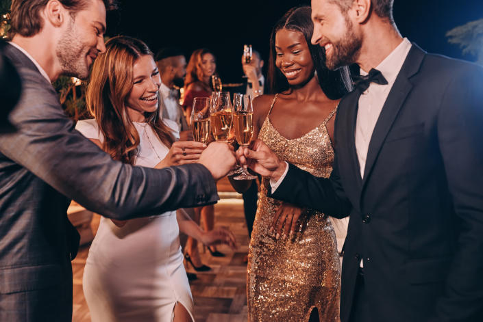 Group of people in formalwear toasting with champagne and smiling while spending time on luxury party