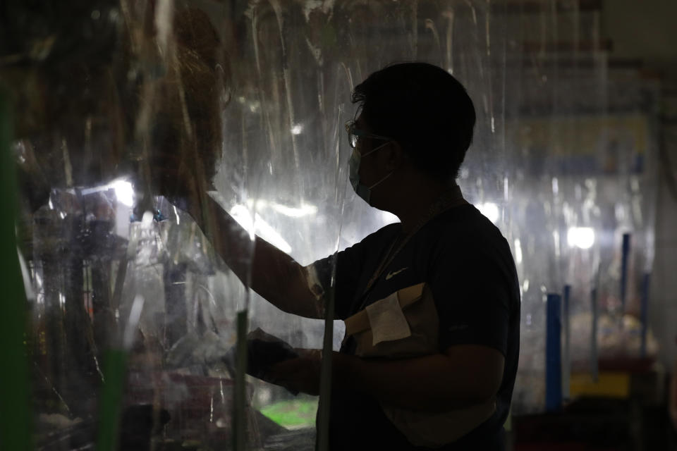 A man wearing a protective mask shops from behind plastic sheets to curb the spread of the coronavirus at a market in Quezon city, Philippines, Tuesday, Sept. 22, 2020. Philippine President Rodrigo Duterte says he has extended a state of calamity in the entire Philippines by a year to allow the government to draw emergency funds faster to fight the COVID-19 pandemic and harness the police and military to maintain law and order. (AP Photo/Aaron Favila)