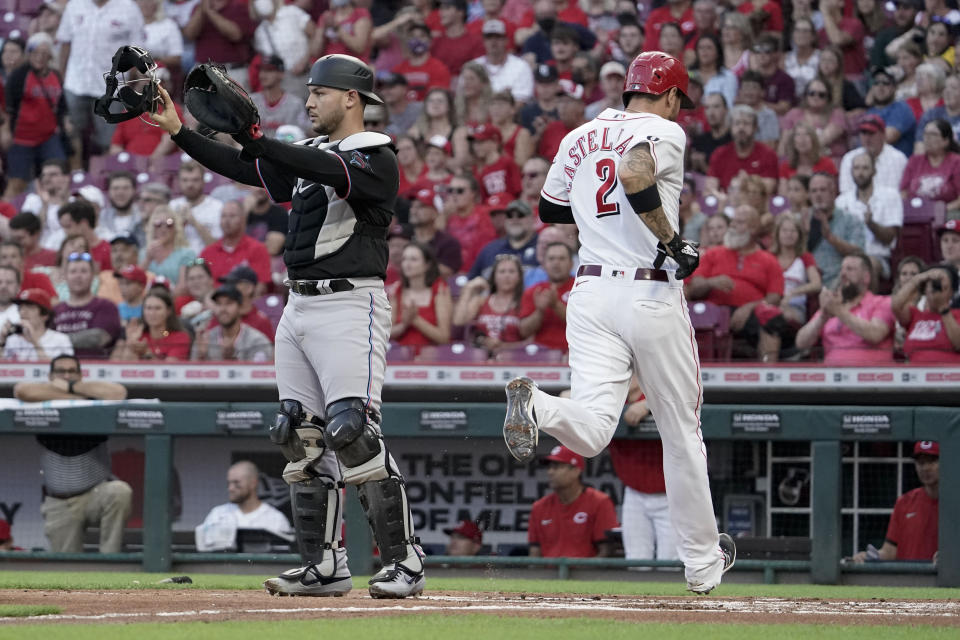 Miami Marlins catcher Alex Jackson, left, motions to teammates as Cincinnati Reds' Nick Castellanos scores off a sacrifice fly ball hit by Kyle Farmer during the first inning of a baseball game Friday, Aug. 20, 2021, in Cincinnati. (AP Photo/Jeff Dean)