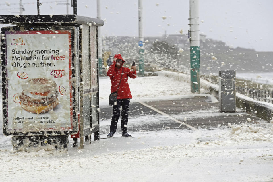 A woman stands as sea foam is brought in by the strong wind in Seaburn, northeastern England, Friday, Oct. 20, 2023. The gale-force winds are expected to hit hardest the eastern part of Denmark's Jutland peninsula and the Danish islands in the Baltic Sea. But the British Isles, southern Sweden, northern Germany and parts of Norway also on the path of the storm, named Babet by U.K.’s weather forecaster, the Met Office. (Owen Humphreys/PA via AP)