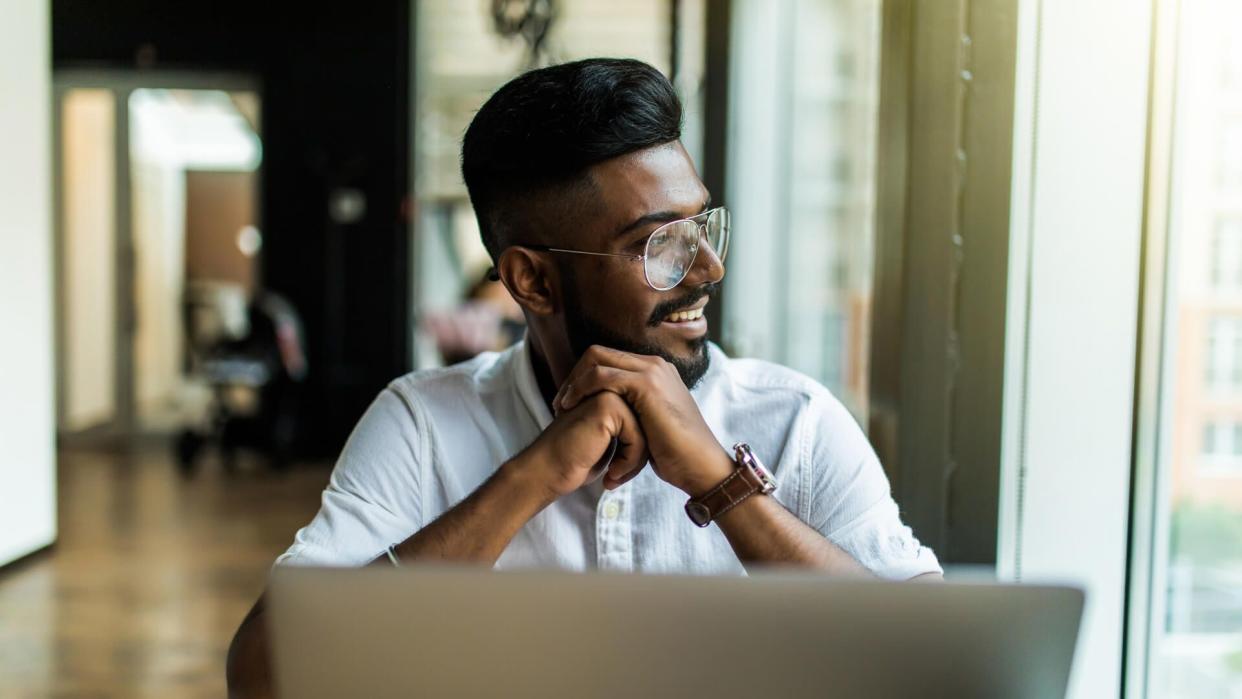 Young Asian Indian businessman using a notebook computer or laptop during office break at cafe, relaxing with a cup of coffee.