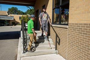 Orientation and Mobility Specialist Garret Waldie teaches LDB Client John N. the technique for safely walking down a staircase using a white cane on Leader Dog’s campus in Rochester Hills, Michigan.