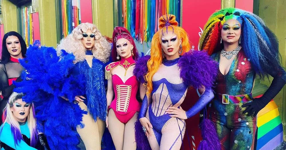 Photograph of drag queens posing in front of rainbow background at Cork LGBTQ+ bar called Chambers