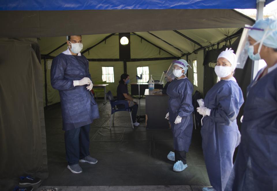 Venezuelan doctors stand at the entrance of a tent set up at the Ana Francisca Perez de Leon hospital for people get a free, quick coronavirus test amid a quarantine to help stop the spread of COVID-19 in Caracas, Venezuela, Wednesday, April 15, 2020. (AP Photo/Ariana Cubillos)