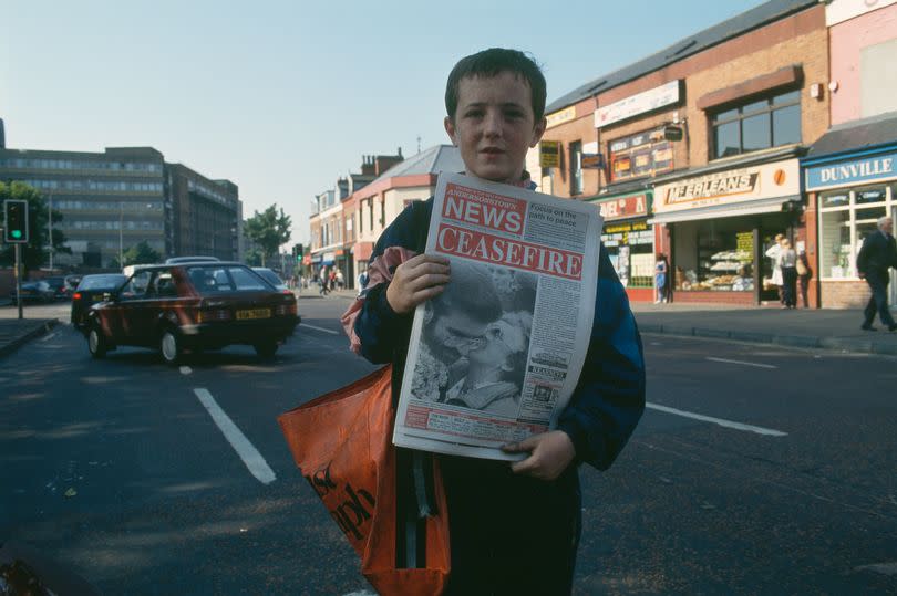 A colour photo of a young boy selling The Andersonstown News on the Falls Road during the ceasefire in Northern Ireland in August 1994