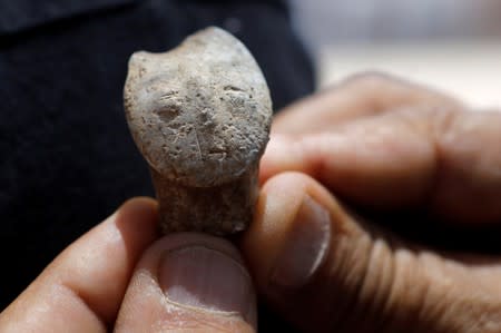 A man holds a figurine depicting a human face, which is part of findings uncovered at a huge prehistoric settlement discovered by Israeli archaeologists, at the excavation site in the town of Motza near Jerusalem