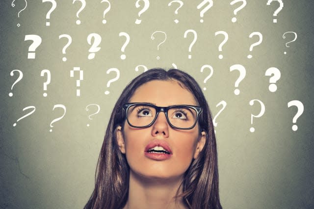 Headshot young beautiful woman with puzzled face expression and question marks above her head looking up isolated on gray wall b