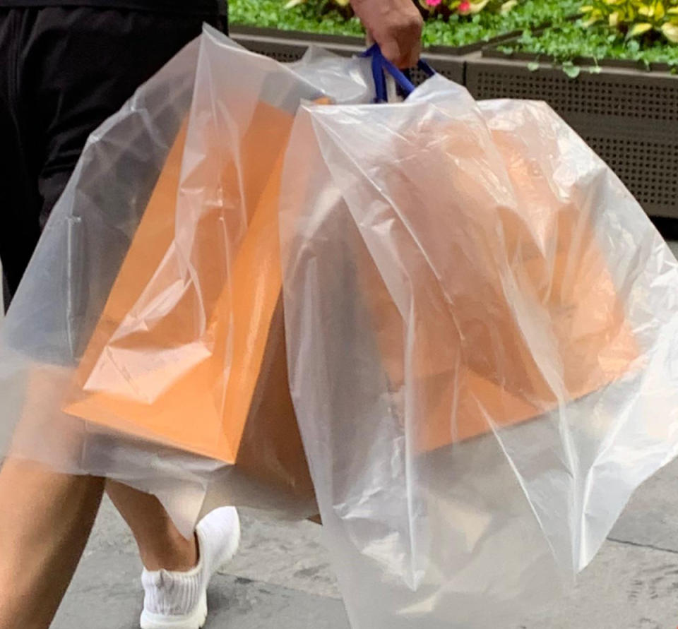 Man walking with Louis Vuitton paper bags covered by plastic bags