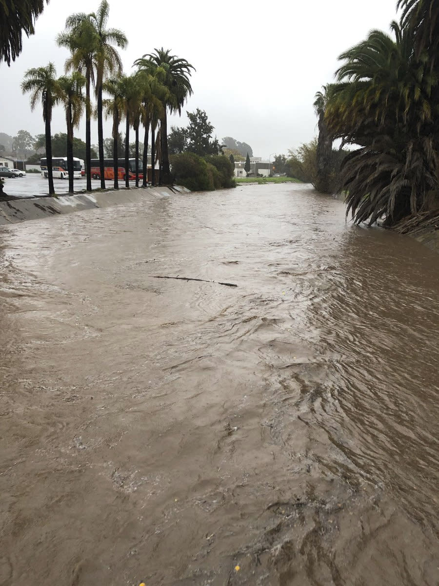 In this Saturday, Feb. 2, 2019, photo released by Santa Barbara County Fire, the San Pedro Creek flows under Hollister Ave. near Fairview Ave. in Goleta, Calif. The second in a string of powerful storms battered California on Saturday, shutting a key highway after water and mud rushed into lanes from bare hillsides in wildfire burn areas that are under mandatory evacuation orders. (Mike Eliason/Santa Barbara County Fire via AP)