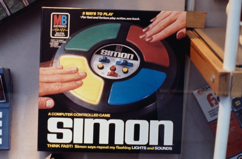 Person's hands playing Simon, a classic electronic memory game with four colored buttons. Retro gaming nostalgia