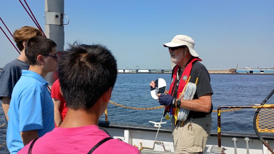 Aboard UWM's research vessel, retired adjunct professor Jim Lubner shows students how to use a Secchi disk to measure how far light penetrates the surface of the water.