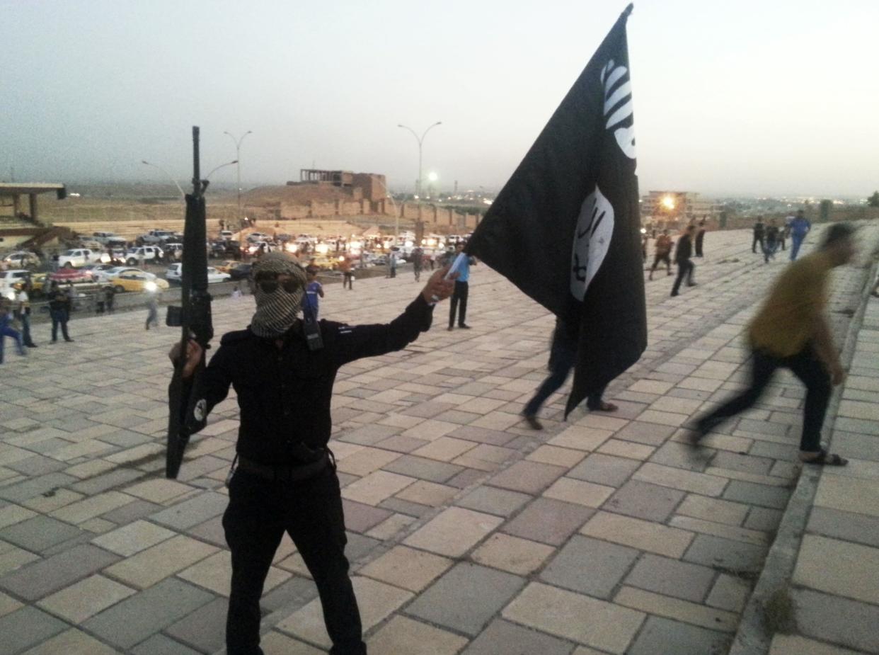 A fighter of the Islamic State of Iraq and the Levant holds an ISIL flag and a weapon in Mosul. (Reuters)