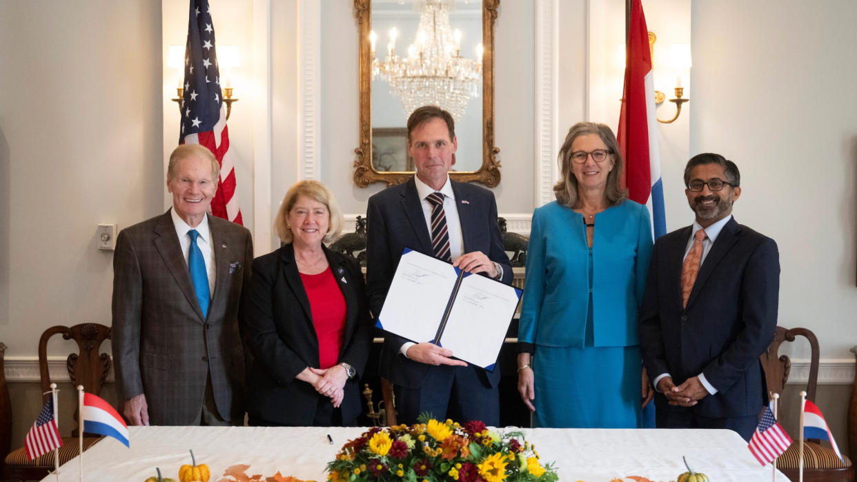  Three men and two women stand behind a white table with the american flag in the background. 