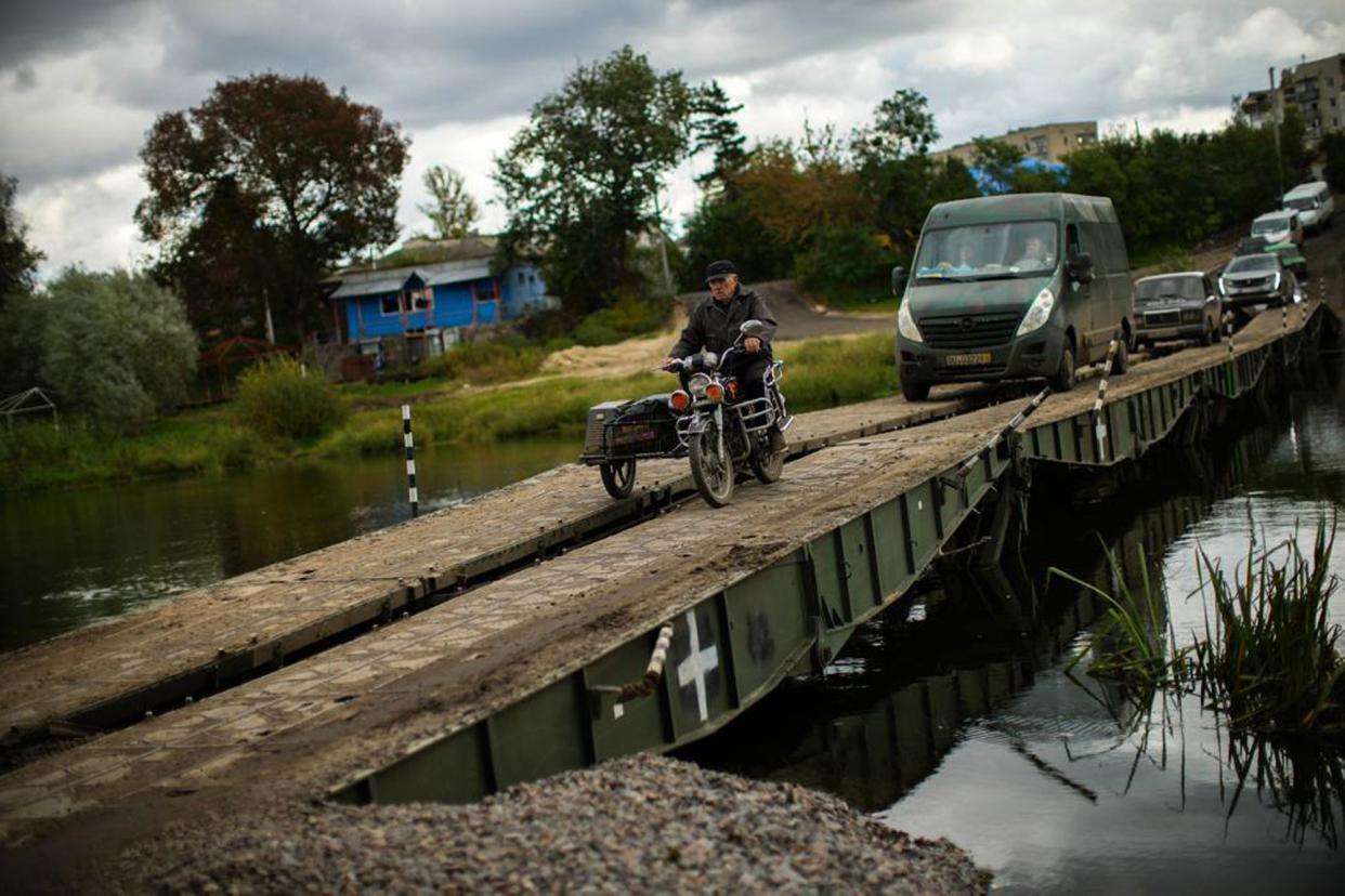 Locals and army vehicles cross a temporary bridge that replaces a destroyed one nearby, in Izium, Ukraine, Monday, Oct. 3, 2022. 