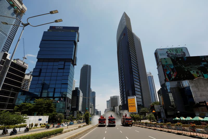 Firefighters spray disinfectant using high pressure pump trucks to prevent the spread of coronavirus disease (COVID-19), on the main road in Jakarta