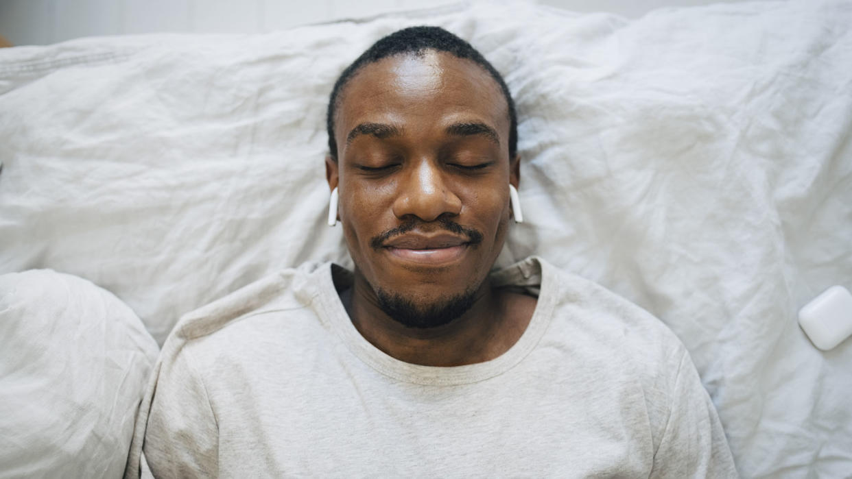  Man lying in bed with eyes closed and Airpods in. 