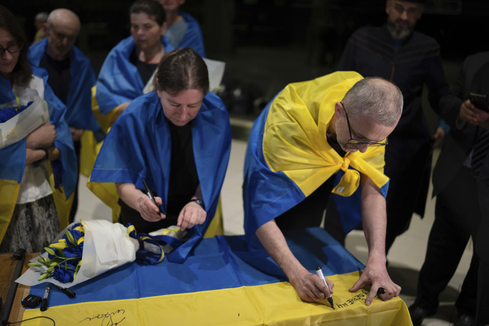 Nariman Dzhelyal (derecha), vicepresidente del Mejlis, o Congreso del Pueblo Tártaro de Crimea, firma una bandera nacional ucraniana en el aeropuerto de Kiev, Ucrania, el 29 de junio de 2024. Diez ucranianos que llevaban años retenidos fueron liberados de su cautiverio ruso con la mediación del Vaticano, según el presidente de Ucrania, Volodymyr Zelenskyy. (AP Foto/Alex Babenko)