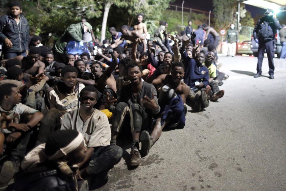 Migrants sit on the ground after storming a fence to enter the Spanish enclave of Ceuta, Spain, Friday, Feb. 17, 2017. An emergency team in Ceuta is assisting more than 300 migrants who crossed the fence surrounding Spain's enclave in North Africa early Friday, a spokesman for the local Red Cross said. (AP Photo/Jesus Moron)