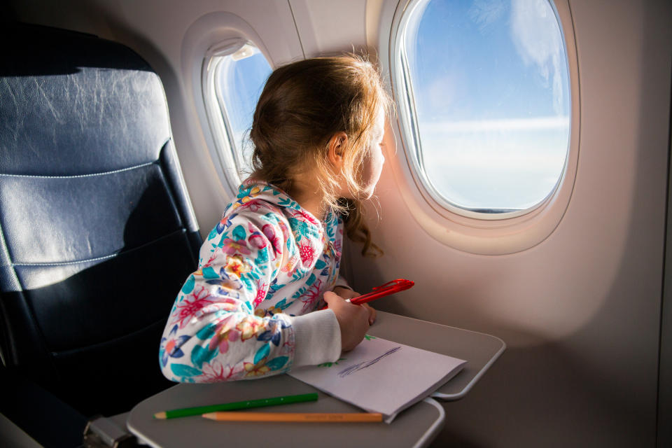 Mädchen, das aus dem Flugzeugfenster schaut, während sie malt.