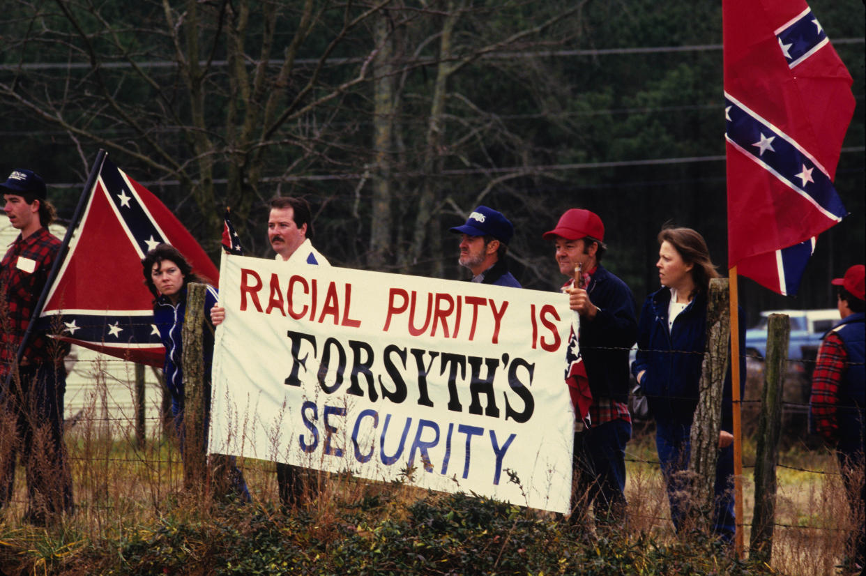 A half dozen Ku Klux Klan supporters hold Confederate flags and a large banner reading: Racial purity if Forsyth's security