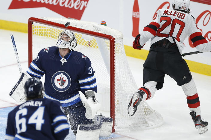 Winnipeg Jets goaltender Connor Hellebuyck (37) looks at the puck on the rebound of a shot by New Jersey Devils' Michael McLeod's (20) during the first period of an NHL hockey game Friday, Dec. 3, 2021, in Winnipeg, Manitoba. (John Woods/The Canadian Press via AP)