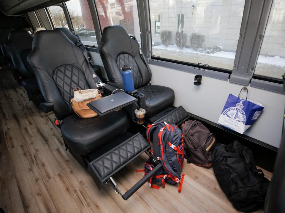 A row of two leather sets. One chair has a laptop, purse, water bottle with bags on the floor.