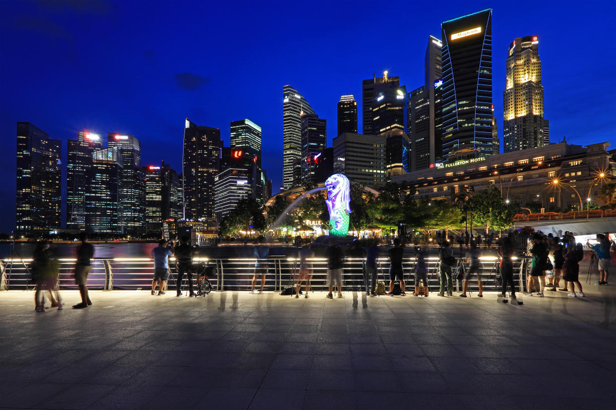 People take photos of the Merlion illuminated with light projection against the Central Business District on December 28, 2021 in Singapore. (Photo by Suhaimi Abdullah/NurPhoto via Getty Images)