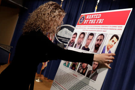 A staff member posts pictures of nine Iranians charged with conducting massive cyber theft campaign before Deputy Attorney General Rod Rosenstein's news conference at the Justice Department in Washington, U.S., March 23, 2018. REUTERS/Yuri Gripas