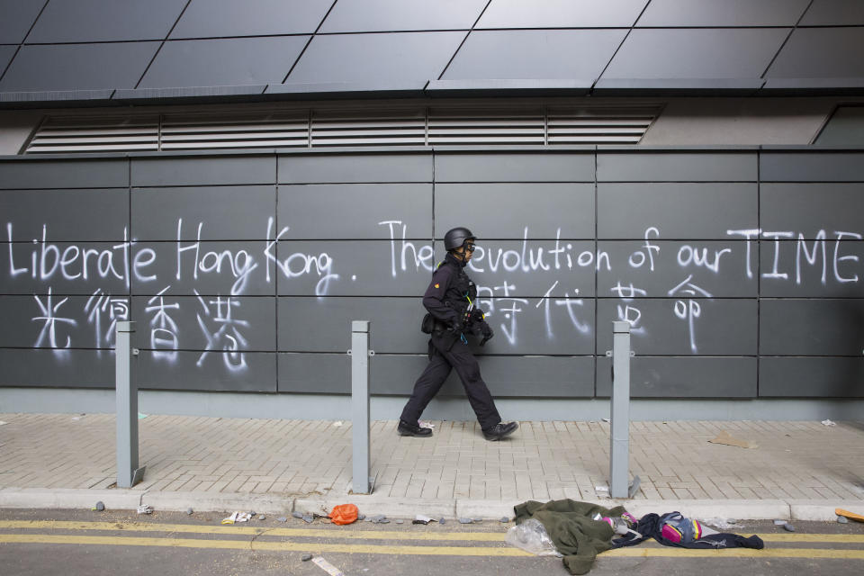 A policeman from Explosive Ordnance Disposal (EOD) unit walks near a wall painted with the words "Liberate Hong Kong, The Revolution of our Times" in Hong Kong, Thursday, Nov. 28, 2019. Police safety teams Thursday began clearing a university that was a flashpoint for clashes with protesters, and an officer said any holdouts still hiding inside would not be immediately arrested. (AP Photo/Ng Han Guan)