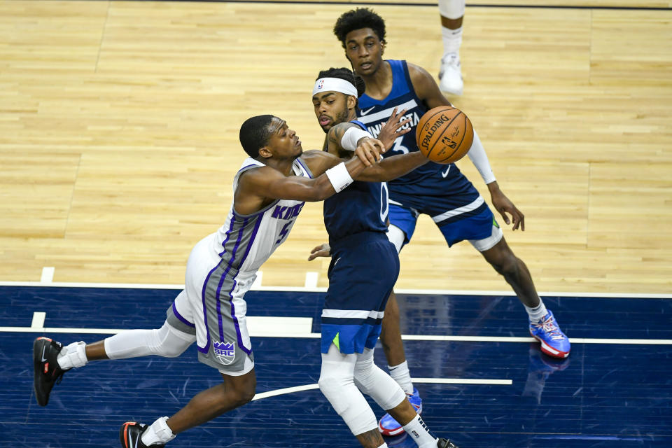 Sacramento Kings guard De'Aaron Fox, left, is fouled by Minnesota Timberwolves guard D'Angelo Russell as Timberwolves forward Jaden McDaniels (3) looks on during the first half of an NBA basketball game Monday, April 5, 2021, in Minneapolis. (AP Photo/Craig Lassig)