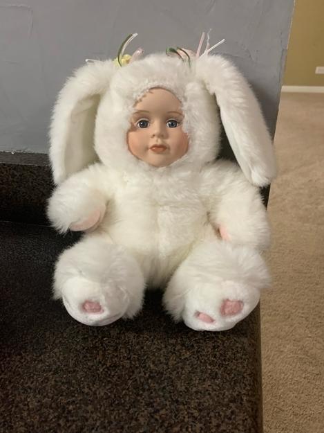 Plush toy resembling a baby with bunny ears and paws sitting on a surface