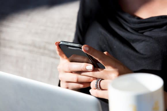 A woman looking at her smartphone while using her laptop