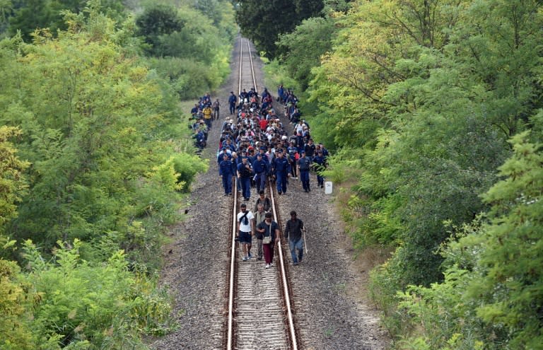 Refugees accompanied by police officers walk on the railway tracks near Szeged town after they broke out from the migrant collection point near Roszke on the Hungarian-Serbian border on September 8, 2015