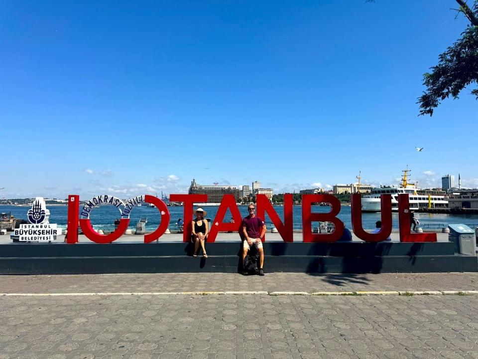 Dorine Olive and her partner, Chuck, sitting in front of a sign that reads Istanbul in red.