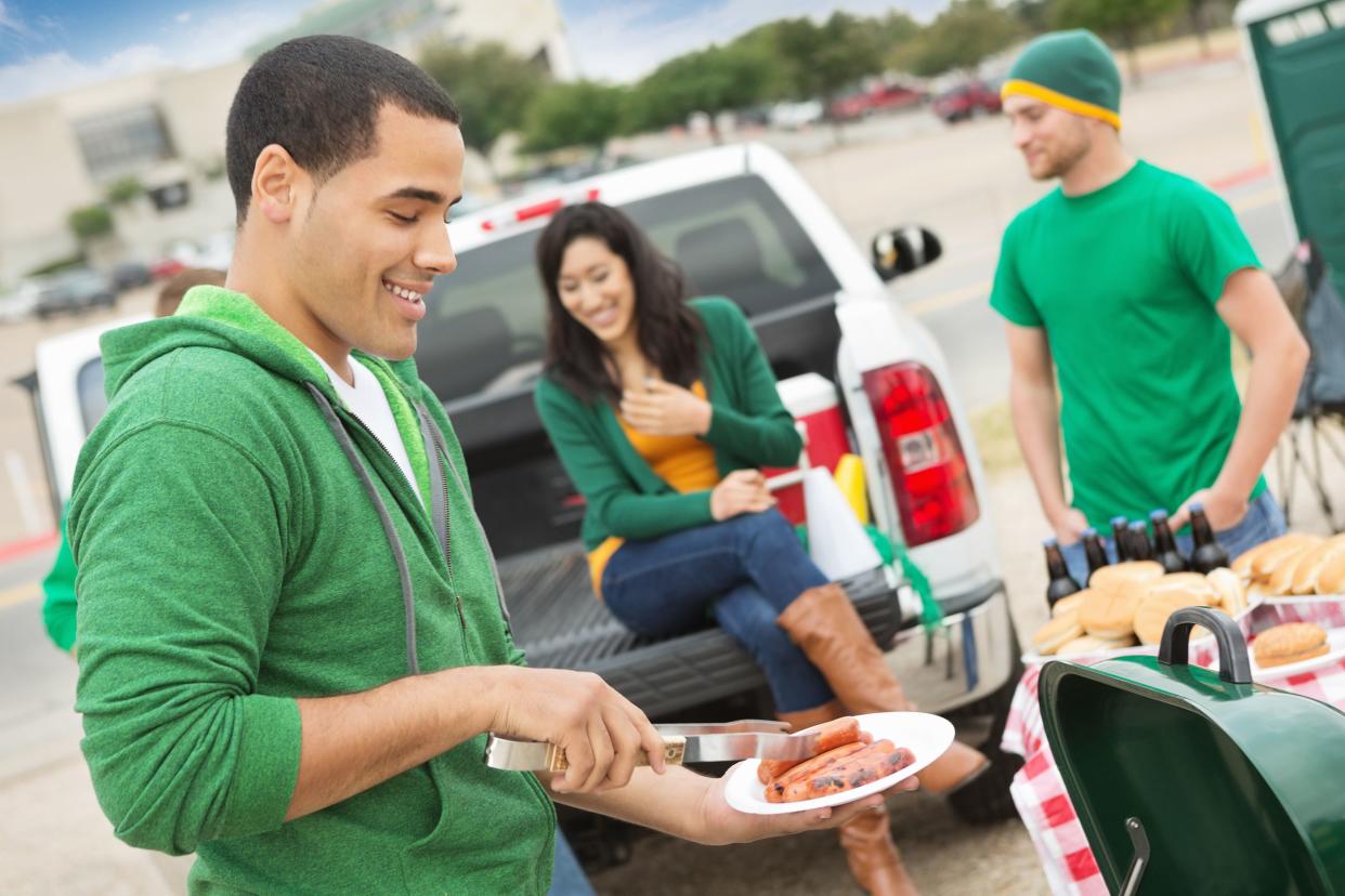 Young man grilling during tailgating party near football stadium.