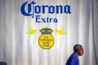 FILE - In this May 18, 2020, file photo, a resident of the township of Soweto outside Johannesburg, South Africa, walks in front of a closed bar advertising Corona beer. A bootlegging culture has sprung up across South Africa in response to the government's nearly 8-week-old ban on the sale of cigarettes and alcohol. The restrictions are part of its lockdown to combat the spread of the coronavirus. (AP Photo/Jerome Delay, File)