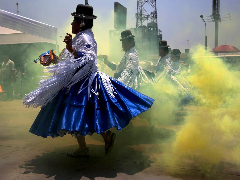 A line of Peruvian dancers in bowler hats, white scarves and blue skirts dance outdoors among a cloud of theatrical yellow dust as part of a pre-feast presentation in honor of Our Lady of Candelaria's upcoming feast day celebrations, in Lima, Peru, Thursday, Jan. 22, 2015.