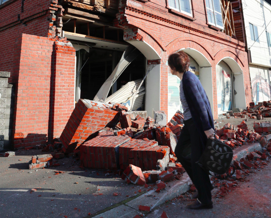 <em>A woman walks past a damaged building in Abira town, near Chitose, Hokkaido (AP)</em>