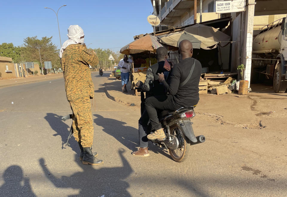 Two men ride past a military checkpoint outside a military base in Burkina Faso's capital Ouagadougou Sunday Jan. 23, 2022. Witnesses are reporting heavy gunfire at a military base raising fears that a coup attempt is underway. Government spokesman Alkassoum Maiga acknowledged the gunfire but denied that the military had taken over the West African country. (AP Photo/Sam Mednick)