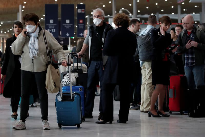 Travellers wearing protective face masks ask for information inside Terminal 2E at Paris Charles de Gaulle airport